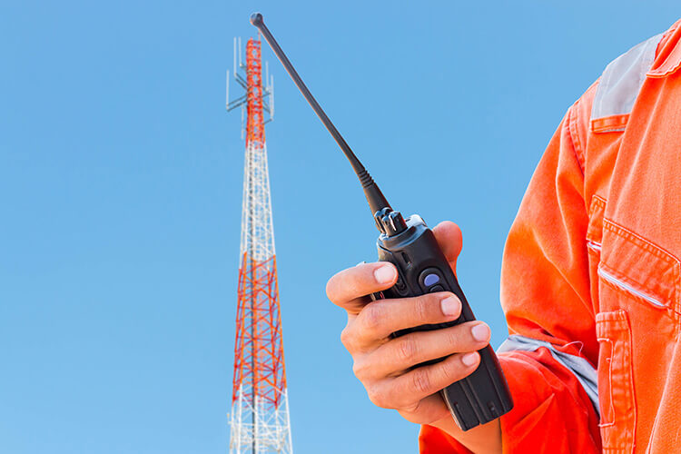 hand holding a radio infront of a radio tower